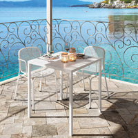 "White outdoor dining set with elegant scrollwork, surrounded by a serene blue sea and sunlit stone patio."