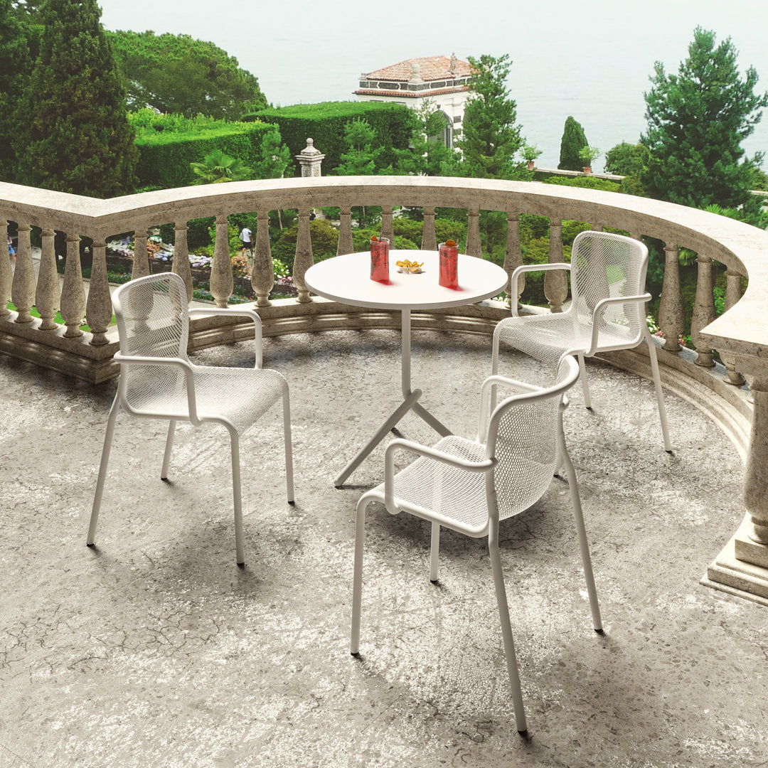 White outdoor chairs and round table on a textured gray patio, surrounded by lush greenery.