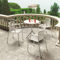 White outdoor chairs and round table on a textured gray patio, surrounded by lush greenery.