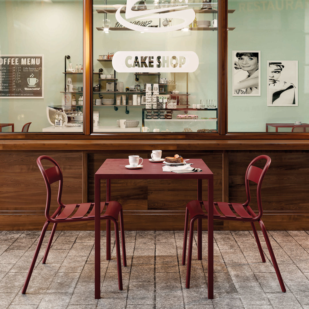 Red metal table with matching chairs, set against a wooden backdrop and pastel-colored shop interior.