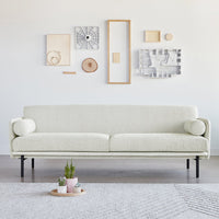 Cream-colored sofa with a textured finish, featuring round side cushions and set against a minimalist wall decor.