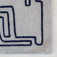 Gray rug with bold navy geometric pattern, featuring a maze-like design for a modern touch.