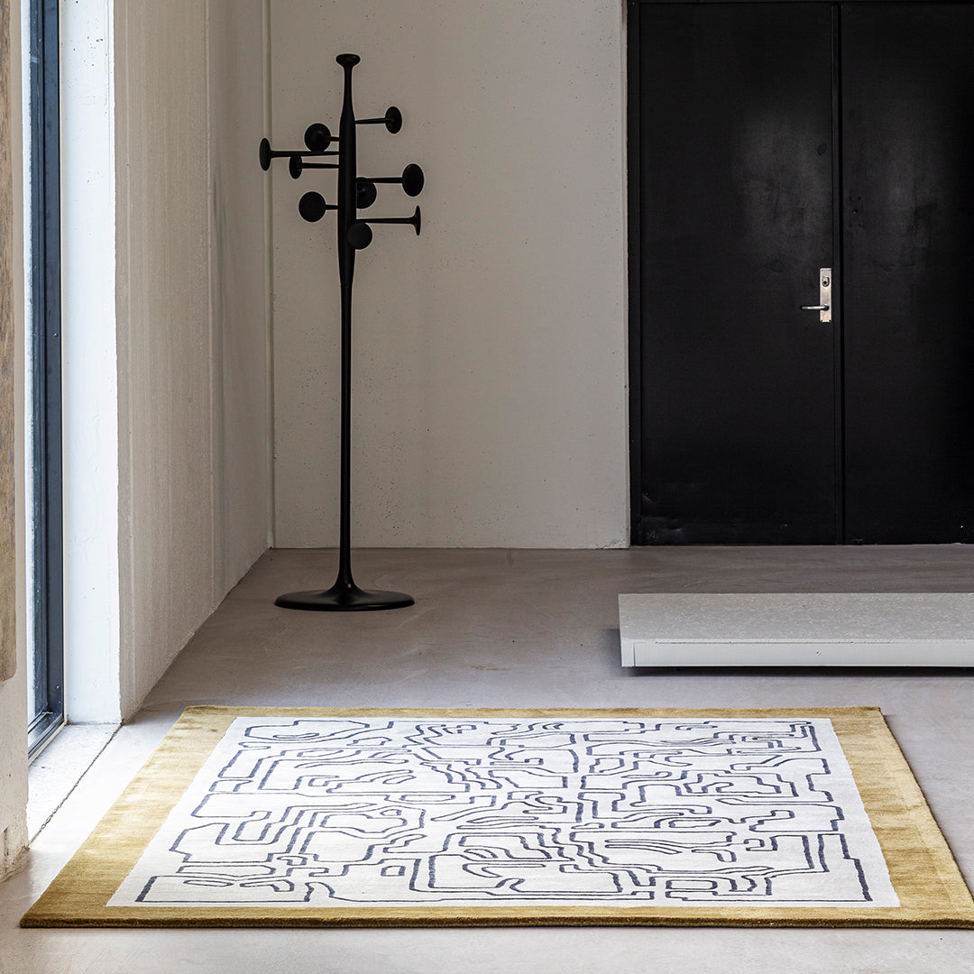"Modern white rug with black geometric patterns and a golden border, perfect for contemporary interiors."