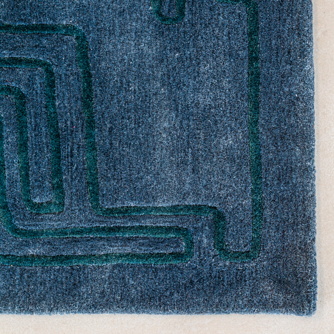 Blue area rug featuring a abstract green geometric pattern. Soft texture with modern design elements.