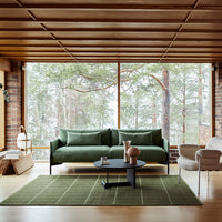 Green sofa with a textured fabric, paired with a patterned green rug and a sleek black coffee table in a warm wood setting.