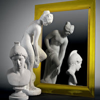 White sculptures with intricate details against a reflective surface, framed by a vibrant yellow mirror.