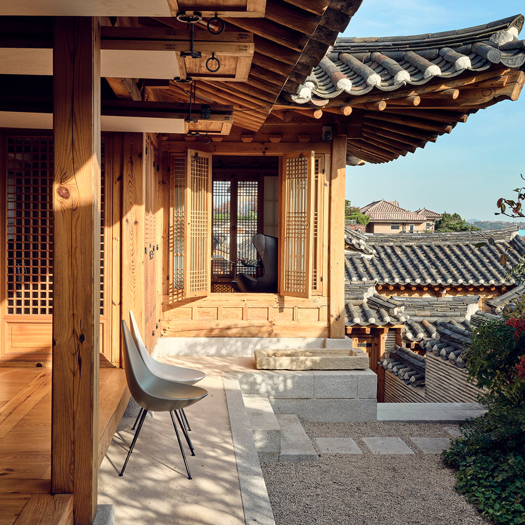 "Modern chair in neutral tones against traditional wooden architecture and blue sky backdrop."