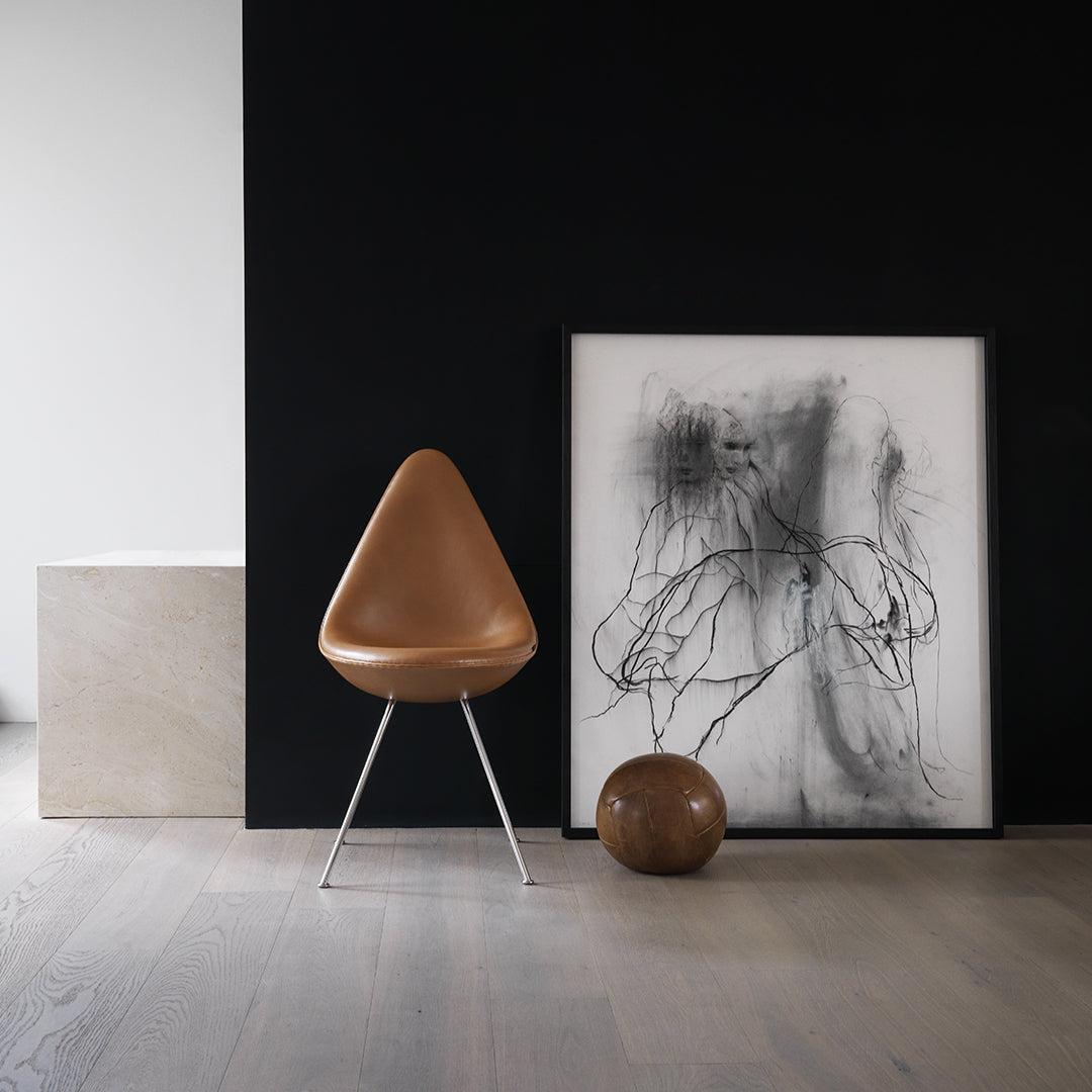Brown chair with sleek design, black wall backdrop, white and black artwork, and a round brown decorative object.