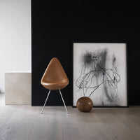 Brown chair with sleek design, black wall backdrop, white and black artwork, and a round brown decorative object.