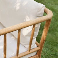 Wooden sofa frame with clean lines and soft, cream-colored fabric cushions on a grassy backdrop.