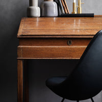 Wooden desk with warm brown tones, black chair, and neutral vase accents against a muted gray backdrop.