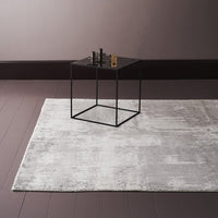 Gray abstract patterned area rug on a dark wooden floor with a black geometric side table.
