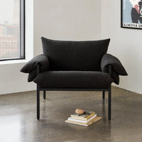 Black textured armchair with plush, oversized cushions and a minimalist metal frame against a modern backdrop.