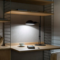 Modern wood desk with sleek metal lamp, warm neutral tones, and soft gray backdrop. Minimalist design with clean lines.