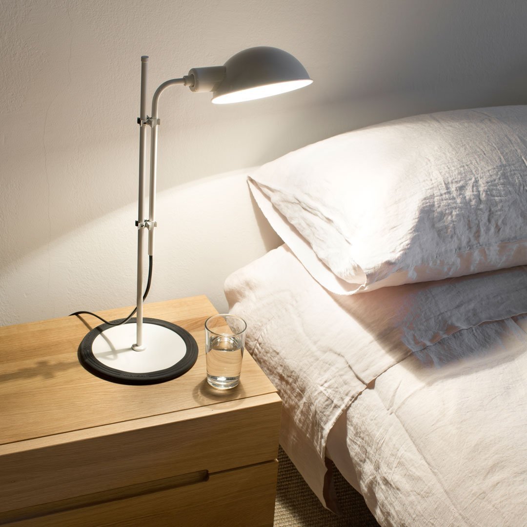 Sleek black and silver desk lamp on a light wood nightstand, complementing soft beige bedding.