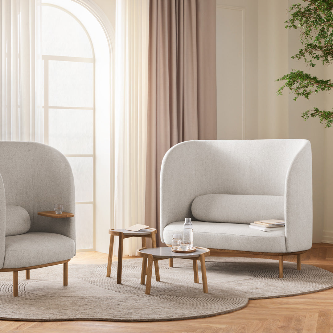 Soft gray armchairs with rounded shapes, wooden legs, layered neutral curtains, and a textured light rug.