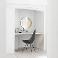 Modern black chair with elegant lines in a minimalist white workspace, featuring a round mirror and subtle natural tones.