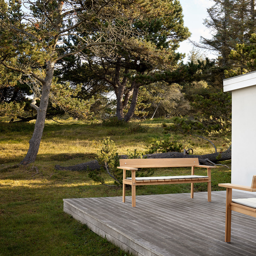 Natural wood bench with a light oak finish, set against lush green grass and textured wooden deck.