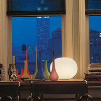 Colorful vases in red, blue, green, and yellow alongside a glowing white lamp against a night city backdrop.
