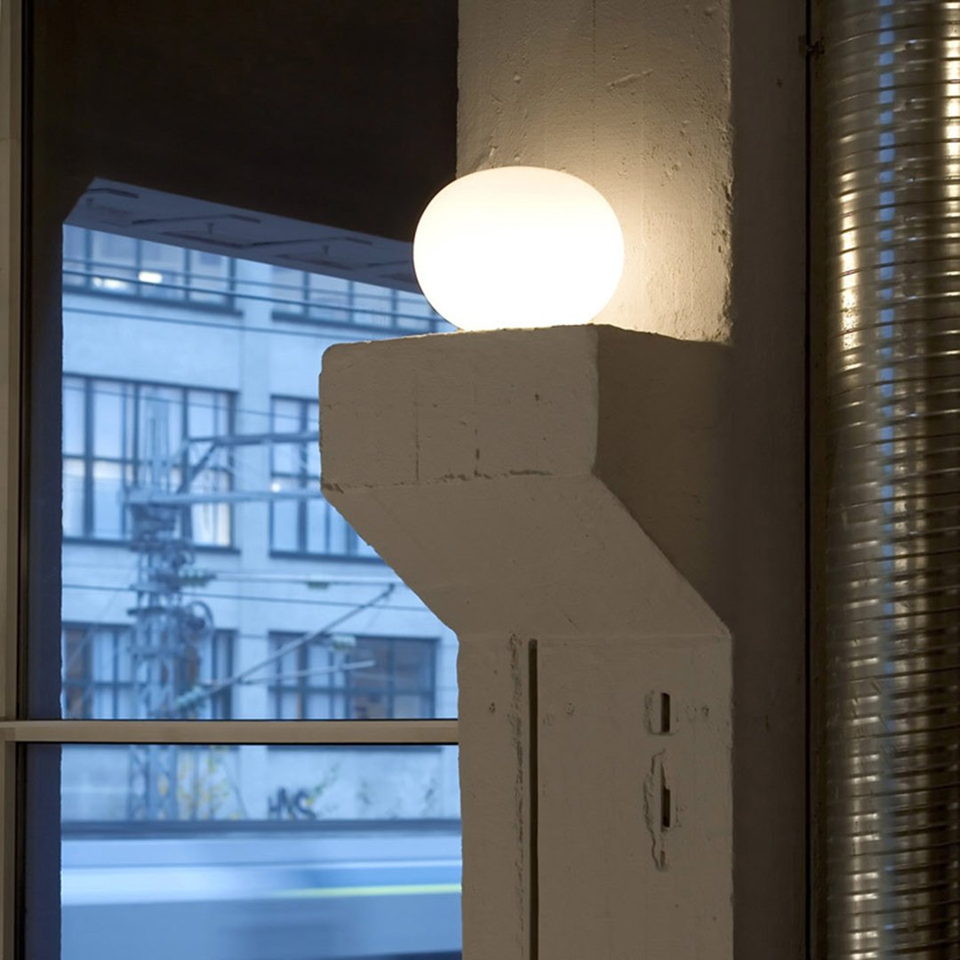 White round lamp on a sleek concrete base with an industrial backdrop of grey and blue hues. Modern minimalist design.