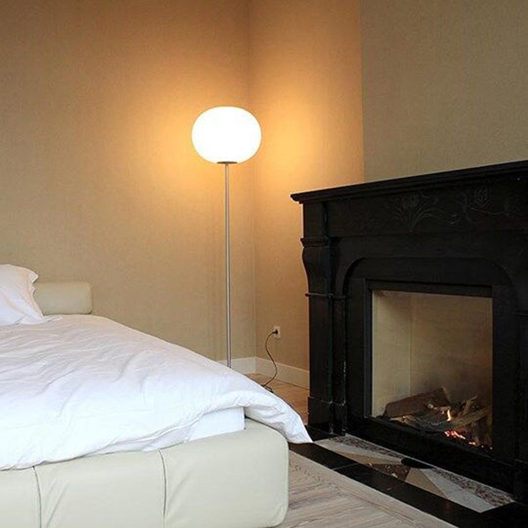 Cozy white bedding on a light beige bed with a sleek black fireplace and soft ambient lighting.