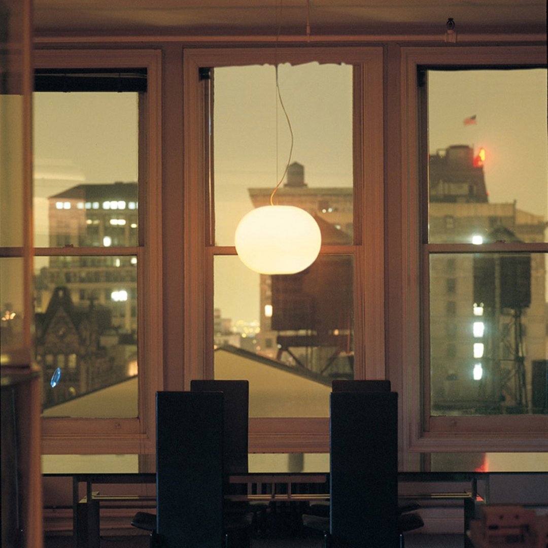 Round white pendant light hanging above a sleek black dining table, framed by city skyline views at dusk.