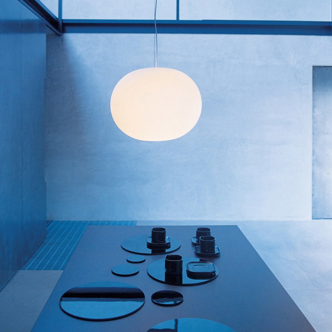 Sleek white pendant light hangs over a modern black table, featuring smooth surfaces and a cool blue backdrop.