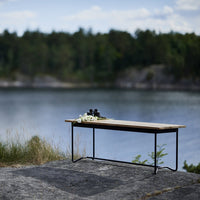 Natural wood tabletop with a grain pattern, contrasted by a sleek black metal frame, set against a serene lakeside backdrop.