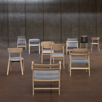 Various modern chairs featuring natural wood tones and gray fabric in a minimalist setting.