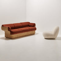 Rust-colored sofa with plush cushions and a woven base, paired with a soft white sculptural chair.