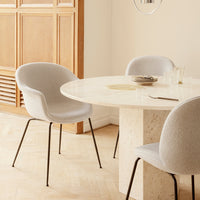 Light gray upholstered chairs around a round beige marble table with subtle textures, set in a warm-toned interior.