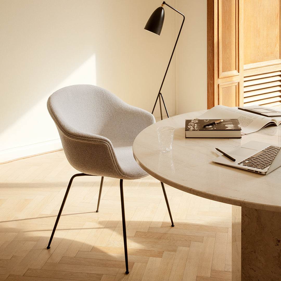 Gray upholstered chair with smooth curves and black metal legs, set against a warm wooden backdrop.