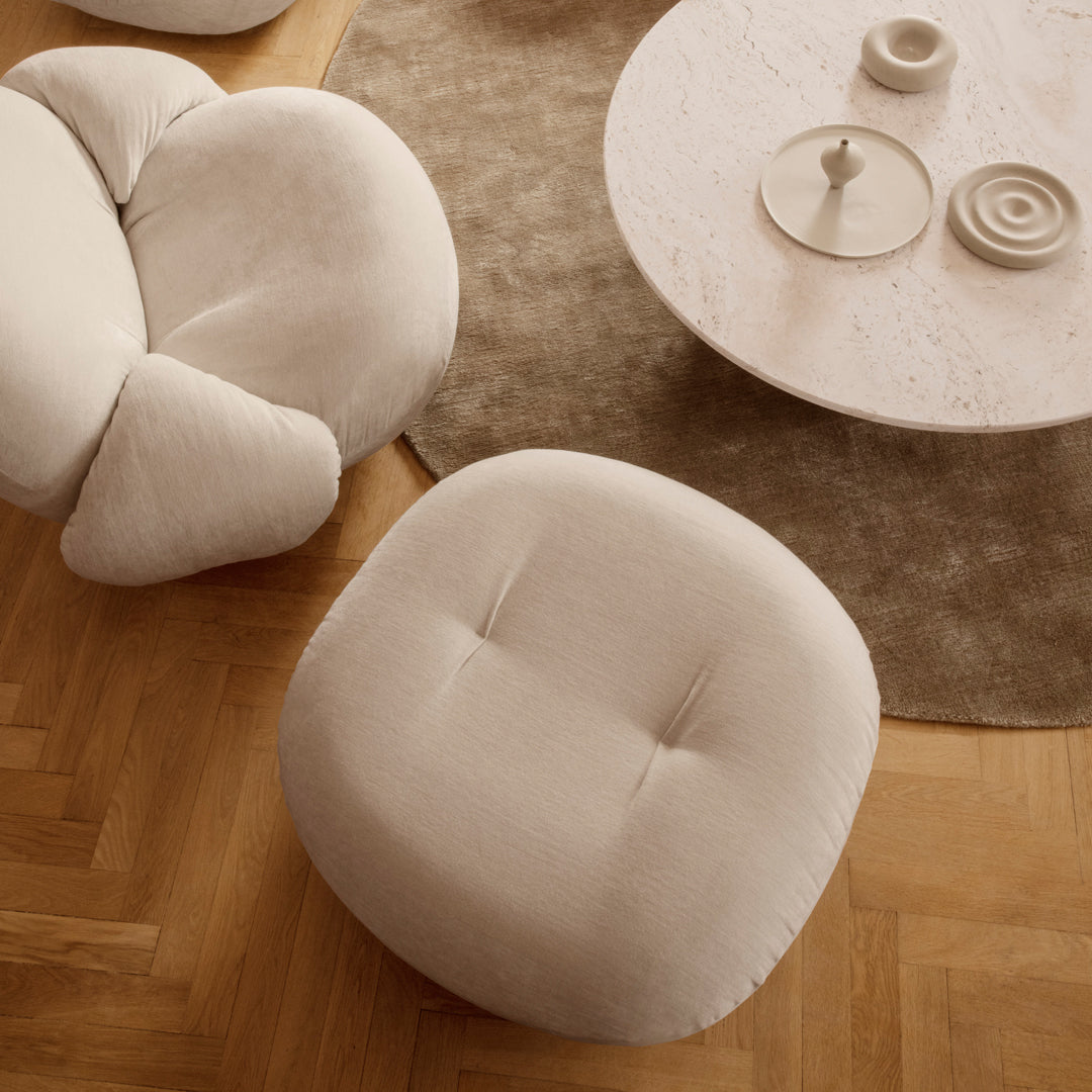 Soft beige upholstered lounge chair and ottoman on a wood herringbone floor, with organic shapes and light neutrals.