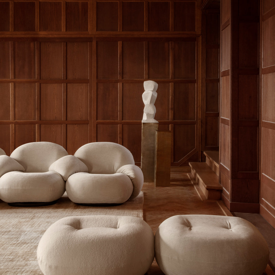 Soft beige round sofas and poufs on a light-toned rug, set against rich wooden paneling for a warm, cozy atmosphere.