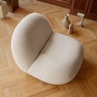 Beige plush chair with a smooth, rounded design, set against a warm wooden floor for a cozy aesthetic.