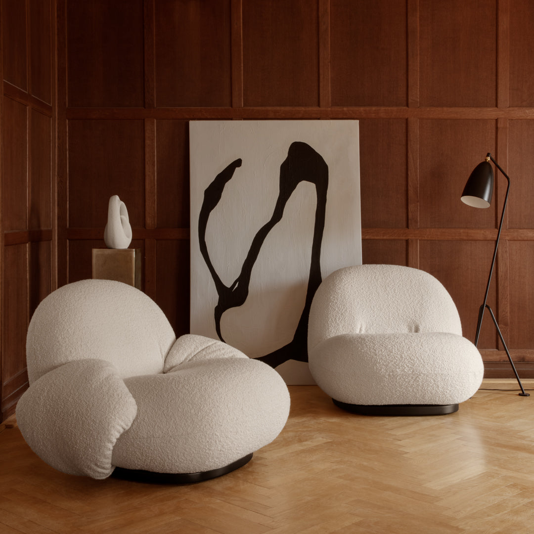 White rounded chairs with textured fabric, set against warm wood paneling and a bold black abstract artwork.