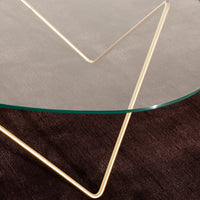 Clear glass tabletop with gold geometric legs on a textured brown surface. Modern and stylish design.