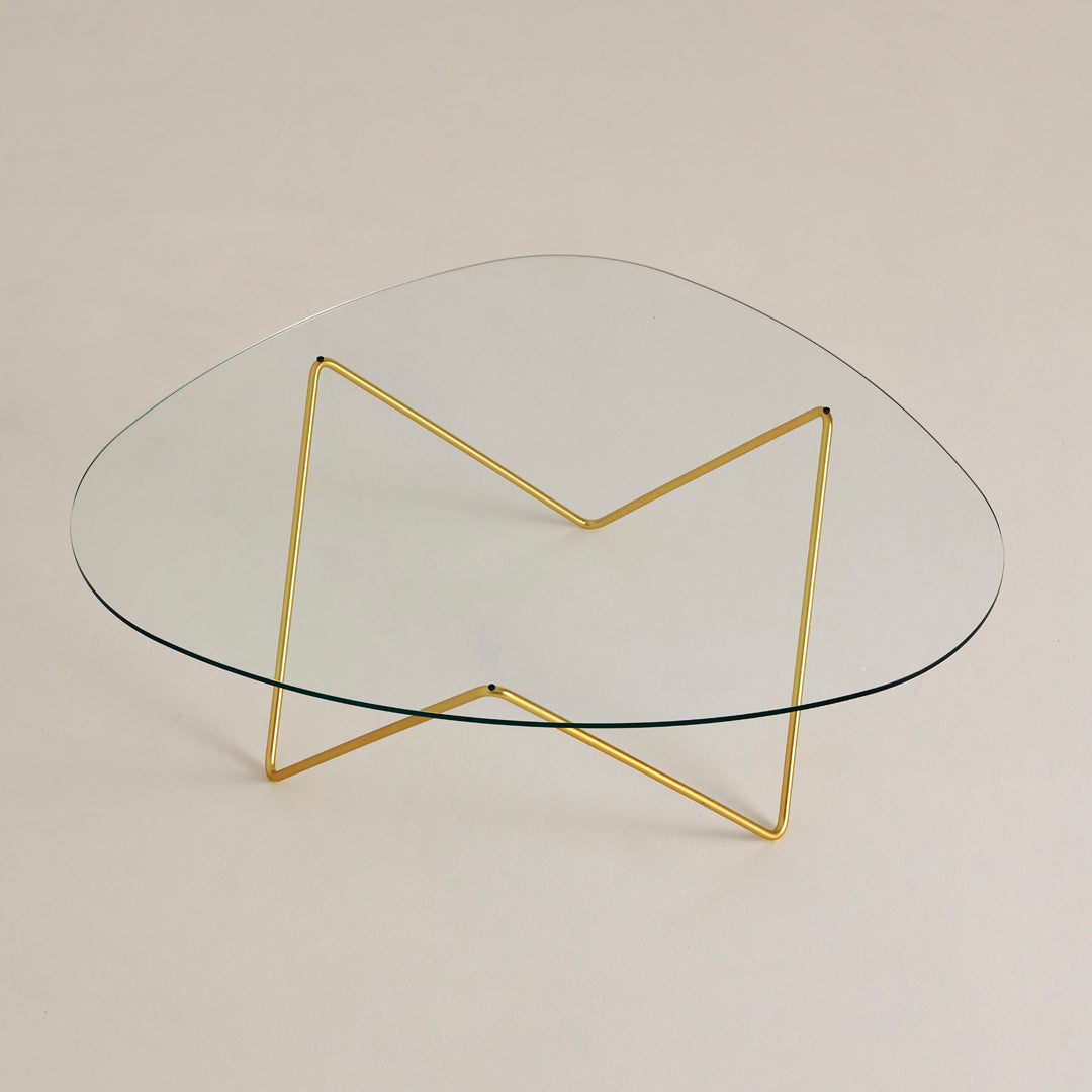 Clear glass tabletop with a unique organic shape, featuring a sleek gold metal base in a geometric pattern.