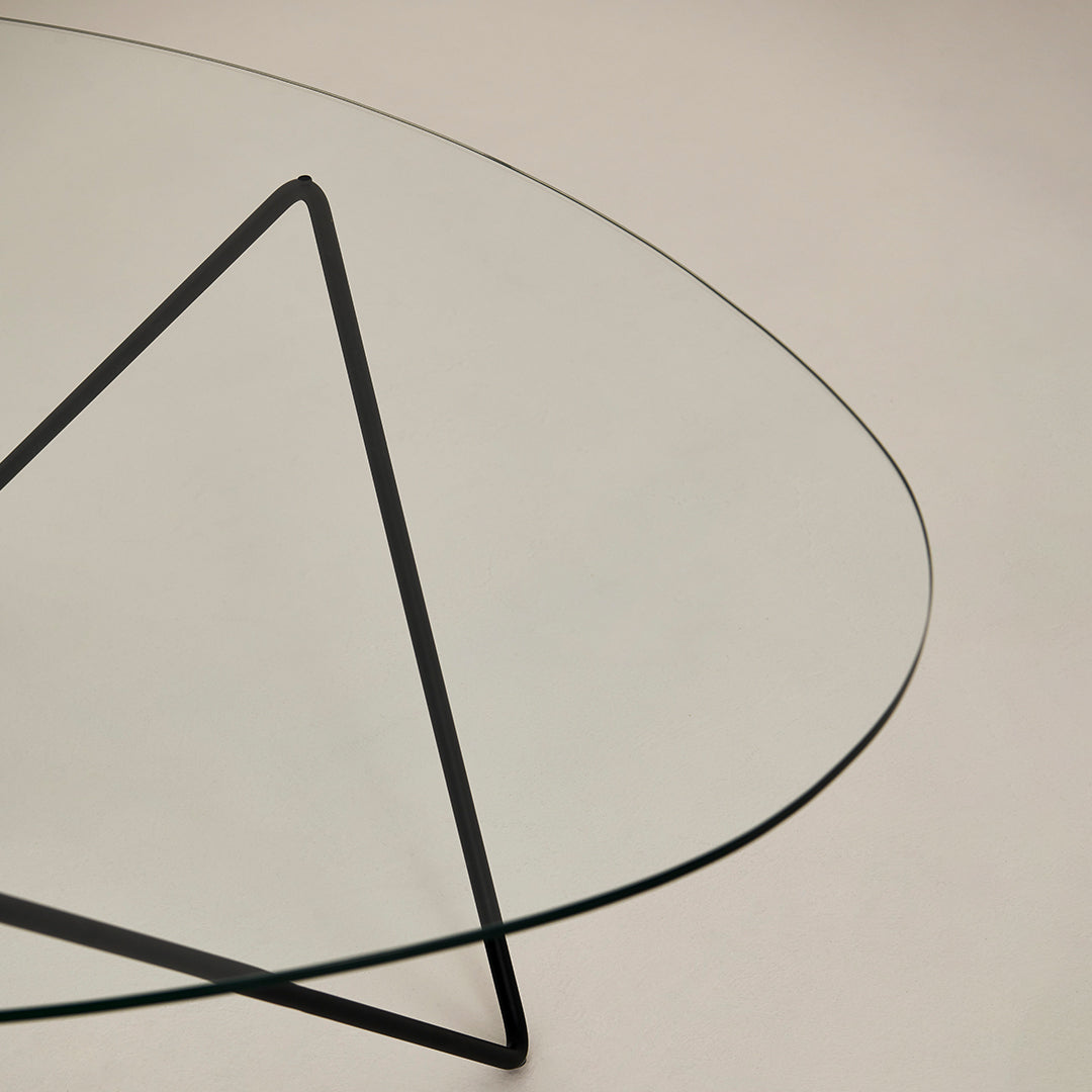 Transparent glass tabletop with a minimalist black triangular metal base, showcasing modern design and clean lines.