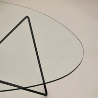 Transparent glass tabletop with a minimalist black triangular metal base, showcasing modern design and clean lines.