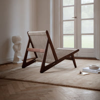 Stylish lounge chair with a natural wood frame and woven beige fabric, against a light, neutral backdrop.
