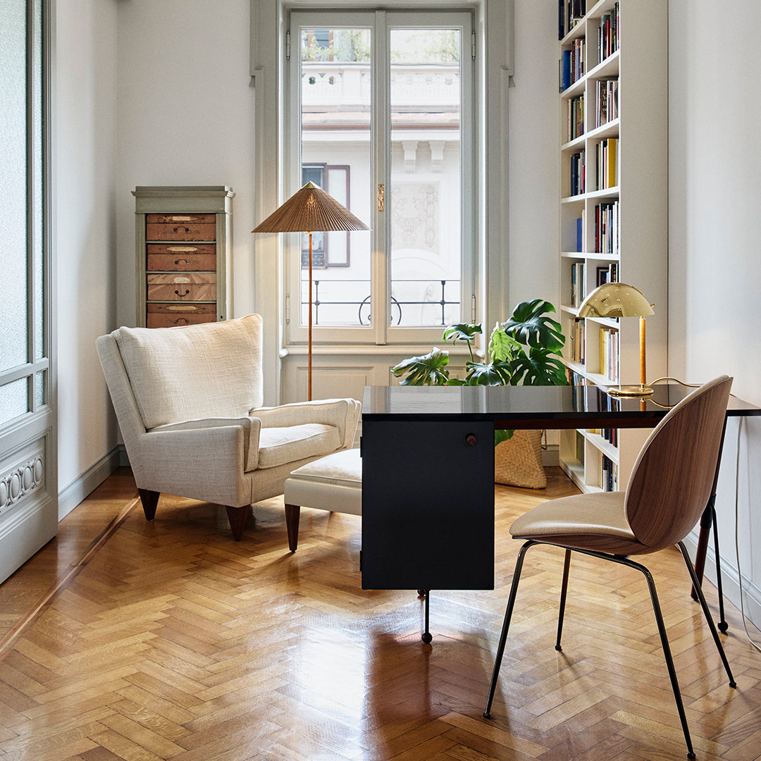 Modern black desk with light wood chair, white armchair, and warm wood herringbone flooring in a bright, airy room.