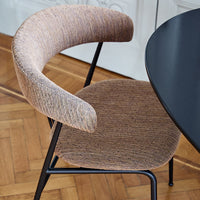 Brown textured chair with curved armrest, paired with a sleek black round table, set against a wooden floor.