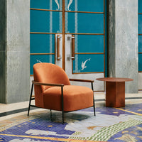 "Rust orange chair on a vibrant patterned rug with blues and greens, paired with a sleek copper side table."