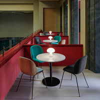 Colorful seating in teal, wood, and gray, with round white lamp on a marble table against a red backdrop.