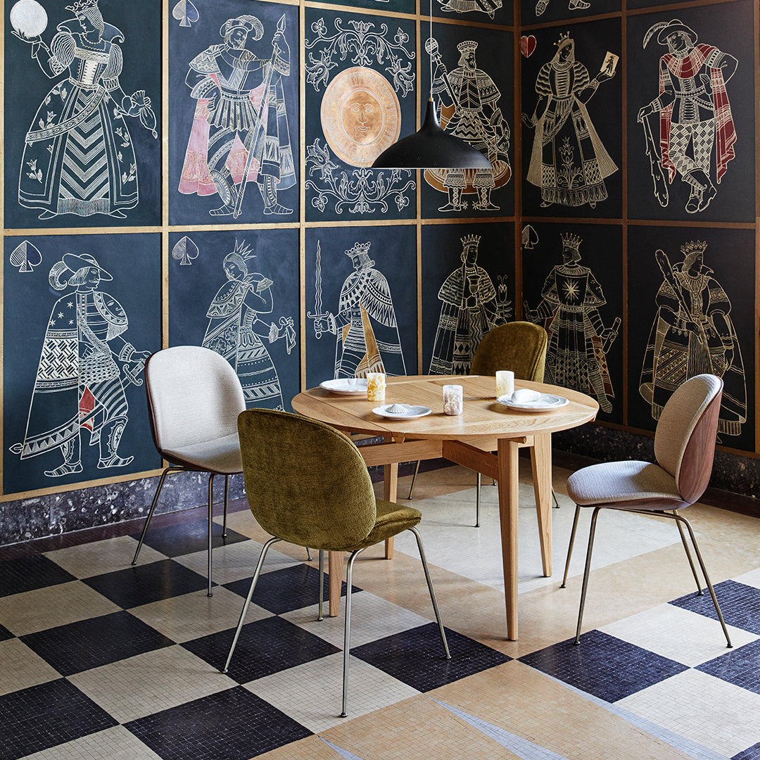 "Stylish dining area with patterned blue wallpaper, beige and olive chairs, and a checkered black and cream floor."