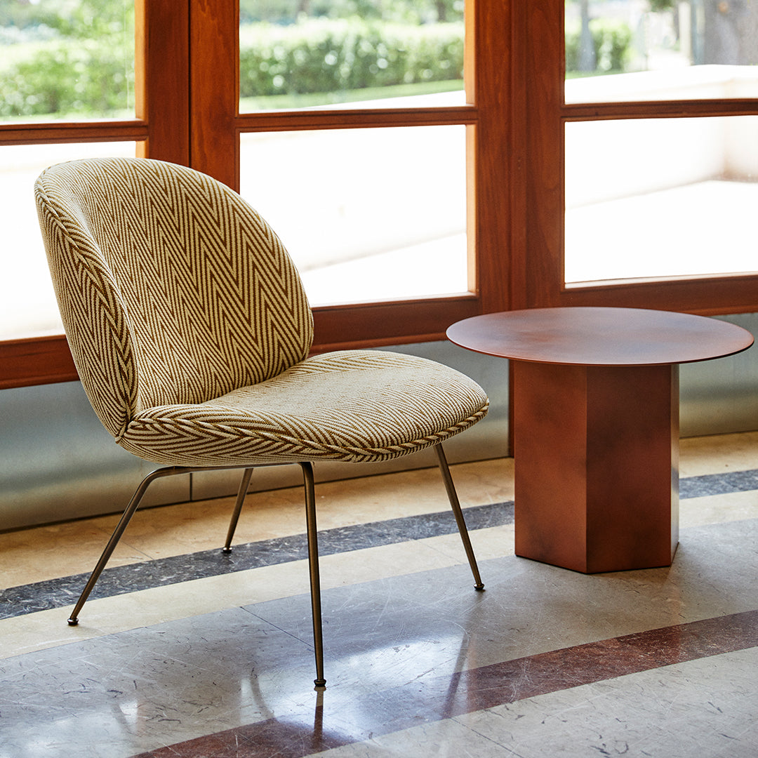 Beige chair with diamond pattern and gold accents, paired with a round, rust-colored side table.