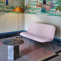 Pink curved sofa with black legs and a round metal table, set against a colorful mural backdrop.