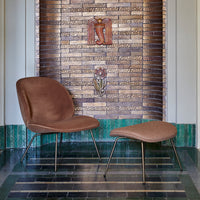 Brown upholstered chair and ottoman set against a patterned brick wall with green and gold accents. Stylish and modern design.