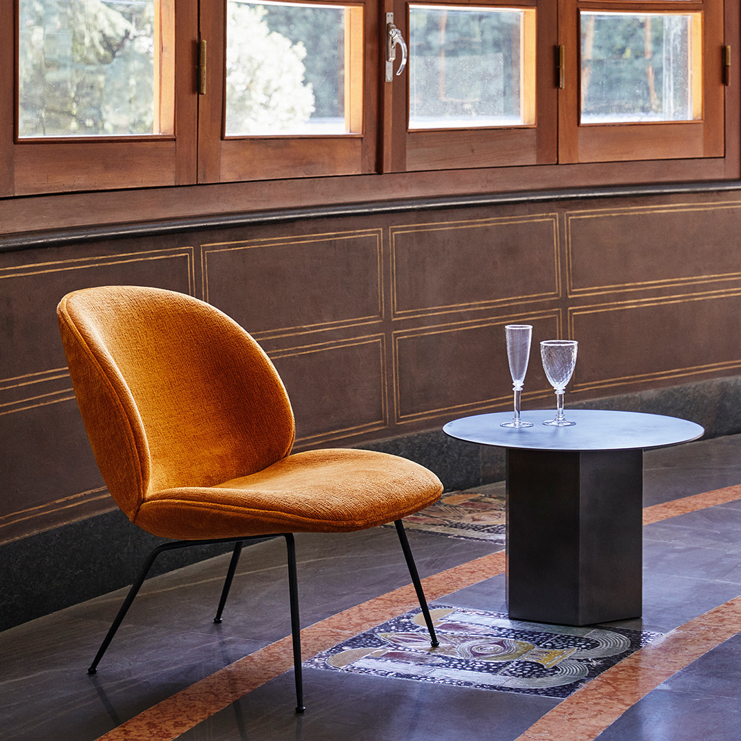 Velvet orange chair with curved design, paired with a sleek round marble top table against elegant wood paneling.